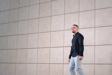 stylish man in light pants and a black shirt on the background of an empty wall takes off in sunglasses looking to the side and holding a mosquito net, dancing and mocking