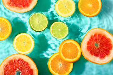Different citrus fruit slices in water on turquoise background