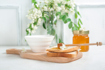 Bowl of honey with flowers of acacia and toasts on light background