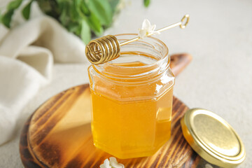 Jar of honey with flowers of acacia and dipper on table, closeup