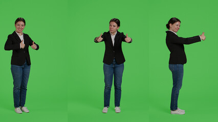 Businesswoman giving thumbs up over green screen studio backdrop, expressing like and approval on camera. Office worker in suit doing okay agreement gesture, acting positive and cheerful.