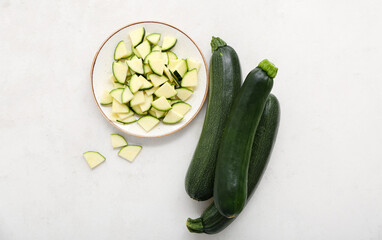 Bowl with slices and fresh green zucchini on white background