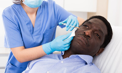 Afro american man getting procedure of injection for face skin tightening in aesthetic clinic