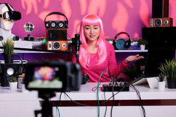 Happy vlogger with pink hair recording podcast while talking with remote subscribers in vlogging studio, posting content on social media. Influencer broadcasting vlog using filming equipment