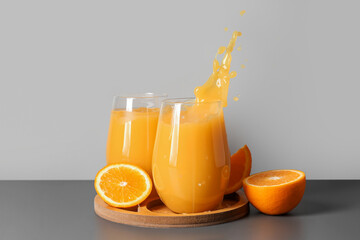 Board and glasses of fresh orange juice with splashes on table against grey background