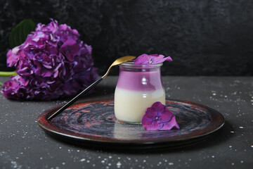 Glass of panna cotta with beautiful hydrangea flowers on black table