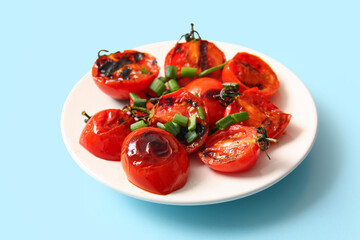 Plate with tasty grilled tomatoes and green onion on blue background
