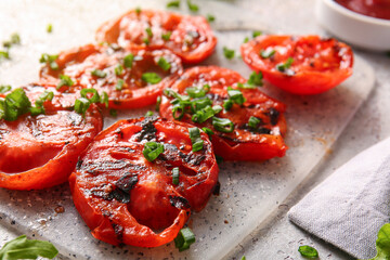 Board with tasty grilled tomatoes and green onion on grey background