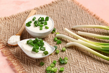 Bowl and gravy boat of tasty sour cream with sliced green onion on pink background