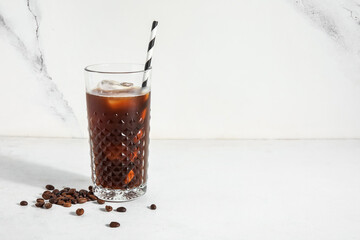 Glass of ice coffee with straw and beans on white table near light grunge wall