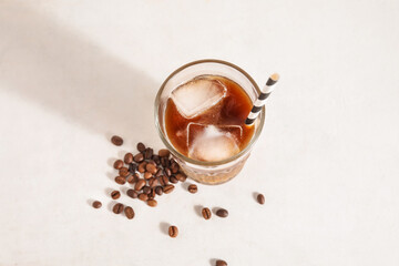 Glass of ice coffee with straw and beans on white grunge background