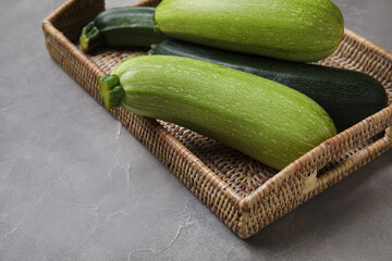 Wicker tray with fresh zucchini on grey background