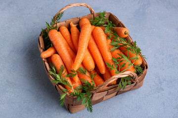 Wicker basket with fresh carrots on blue background