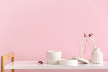 Holders with candles and decor on table near pink wall in room
