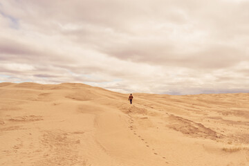 Fototapeta na wymiar Lone man walking under the clouds across the sand at Great Sandhills Ecological Reserve