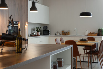Interior of modern kitchen with dining table, island and glowing lamps