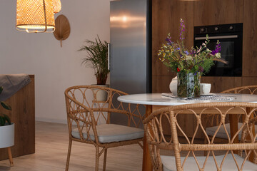 Interior of modern kitchen with glowing lamp and flower vase on dining table