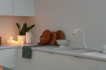 White counters with burning candles and sink in interior of kitchen at evening