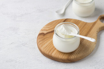 Natural homemade yogurt in a glass jar on a wooden board on a light gray background