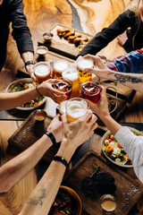 Friends cheering beer glasses on wooden table covered with delicious food - Top view of people having dinner party at bar restaurant - Food and beverage lifestyle concept - 613664452
