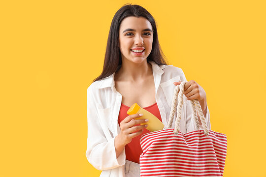 Young Woman Putting Sunscreen Cream In Beach Bag On Yellow Background