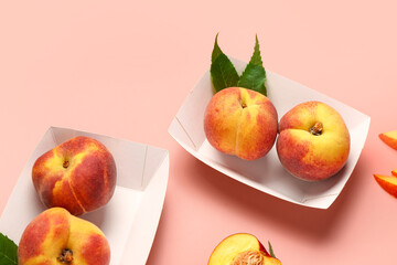 Paper plates with sweet peaches and leaves on pink background