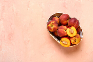 Wicker bowl with sweet peaches on pink background