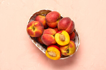 Wicker bowl with sweet peaches on pink background