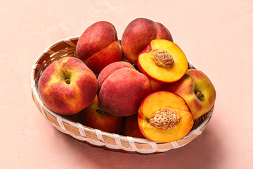 Wicker bowl with sweet peaches on pink background