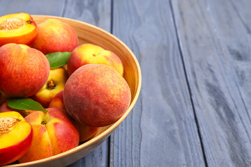 Bowl with sweet peaches and leaves on blue wooden background
