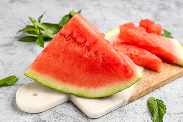 Board with pieces of fresh watermelon and mint on grey background