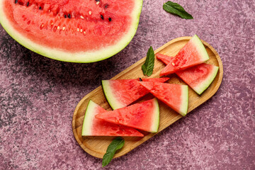 Half of fresh watermelon and board with pieces on purple background