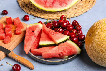 Plate with pieces of fresh watermelon and cherries on blue background