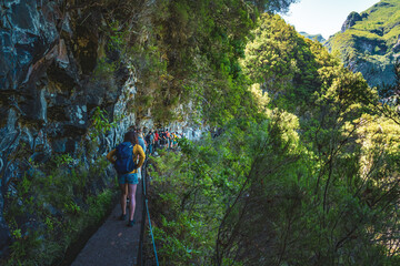 Tourist group walking along steep cliff jungle hiking trail  next to canal through Madeiran...