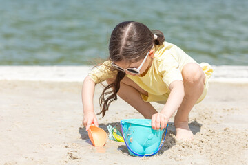 Little girl playing on the beach on summer holidays. Child having fun with a sand on the city lake seashore. Vacation concept. Happy sunny day