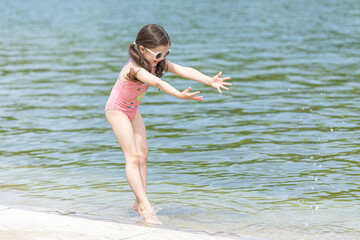 Naklejka premium Little girl playing on the beach on summer holidays. Child having fun with a sand on the city lake seashore. Vacation concept. Happy sunny day