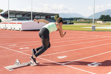 Young woman preparing for the run race, taking a start position for sprint, using starting block