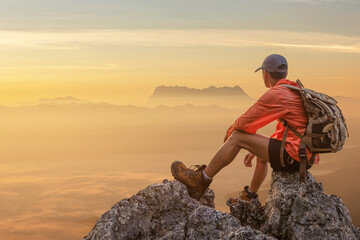 Hipster male hiker with backpack enjoying sunset on peak of foggy mountain. Tourist traveler on...