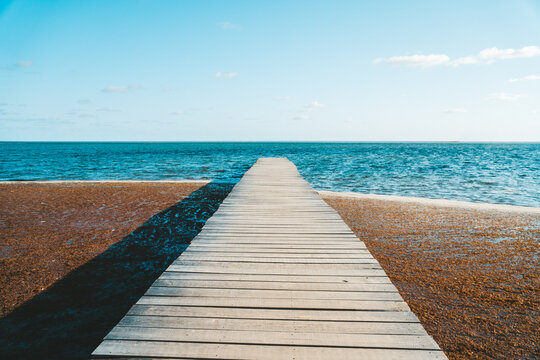 Wide shot showing a pier leading to a the ocean on Cozmel island in Mexico. Contrasting colours shown. © Sam