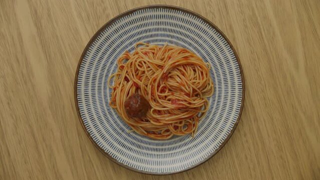 top view of plate of pasta in tomato sauce rotating with a meatball