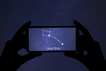 Woman using stargazing app on her phone at night, closeup. Identified stick figure pattern of...