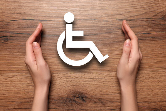 Disability inclusion. Woman protecting wheelchair symbol on wooden background, closeup
