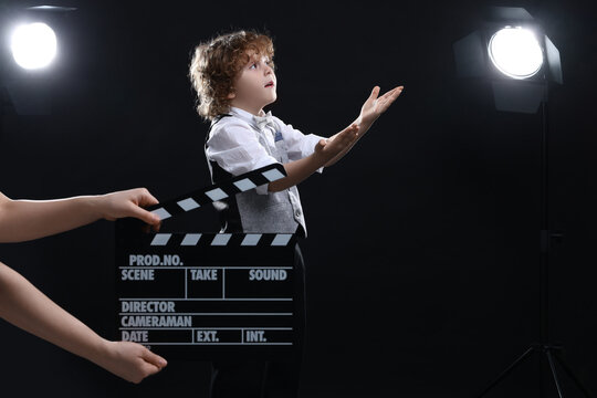 Cute boy performing while second assistant camera holding clapperboard on stage. Little actor