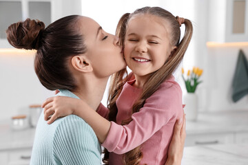 Happy mother kissing her cute daughter in kitchen