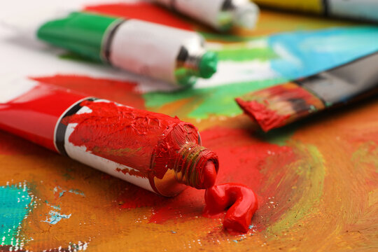Tube of red oil paint on canvas with abstract painting, closeup