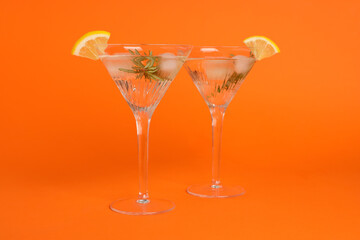 Martini glasses of refreshing cocktail with lemon slices and rosemary on orange background