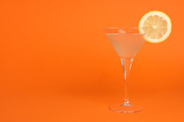 Martini glass of refreshing cocktail with lemon slice on orange background, space for text