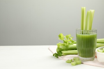Glass of celery juice and fresh vegetables on white table, space for text