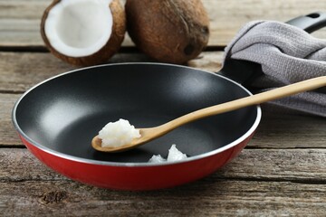 Frying pan with organic coconut cooking oil and spoon on wooden table, closeup