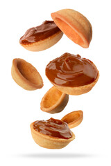 Many empty and filled with caramelized condensed milk nut shell shaped cookie parts falling on white background